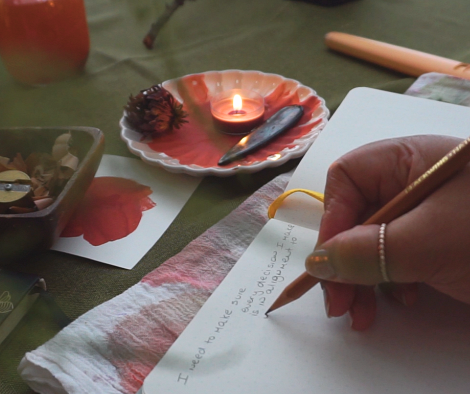 artist desk with paint palette and red paint inside. also a candle. artist is writing in her studio journal