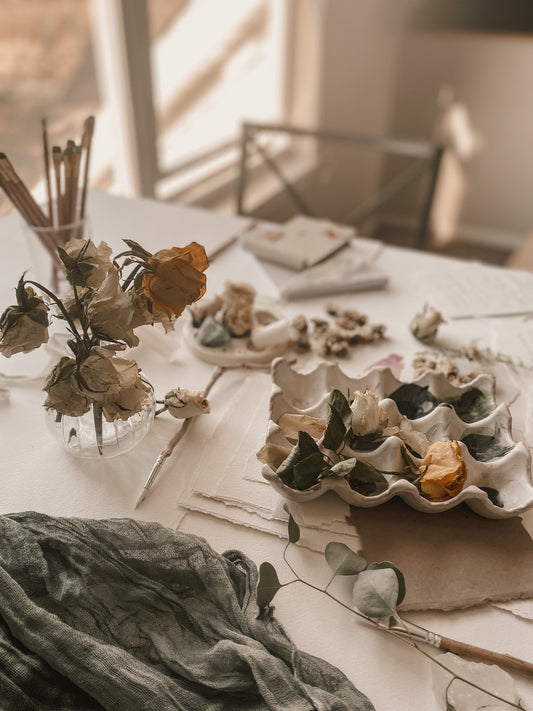 Artist desk with dried florals, paint palette, white paper and pencils