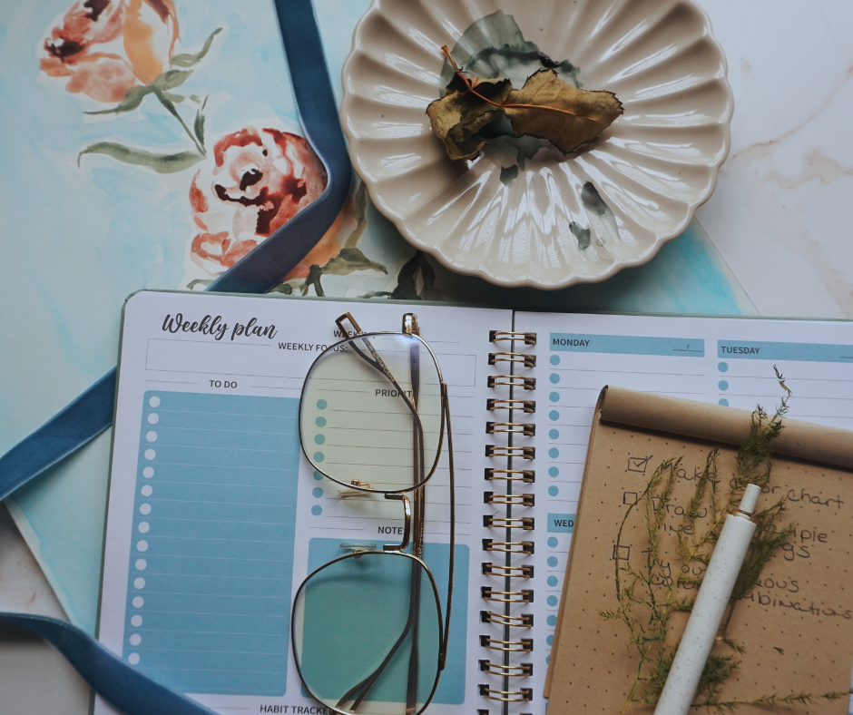 artist desk with watercolor artwork of roses, a paint palette, a weekly planner and a pen